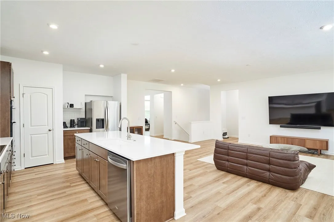 Kitchen with appliances with stainless steel finishes, a sink, light wood-style flooring, open floor plan, and an island with sink