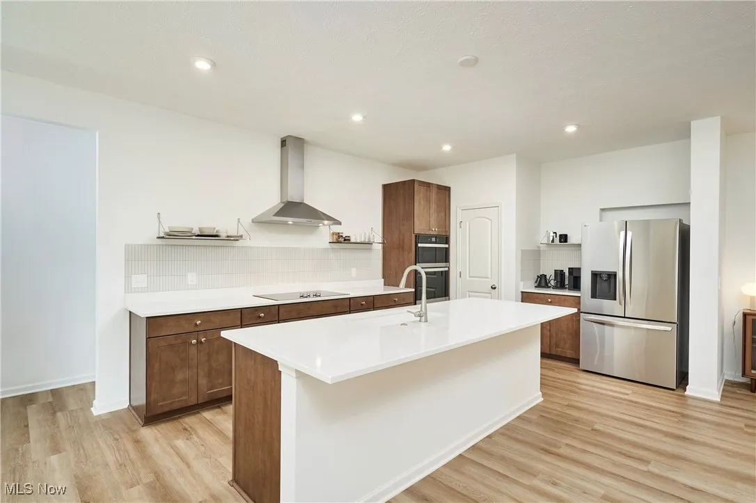 Kitchen featuring black appliances, wall chimney range hood, open shelves, light wood-style floors, and recessed lighting