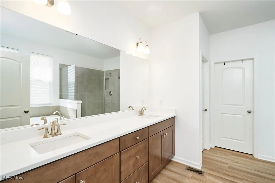 Bathroom featuring double vanity, wood finished floors, tiled shower, and baseboards