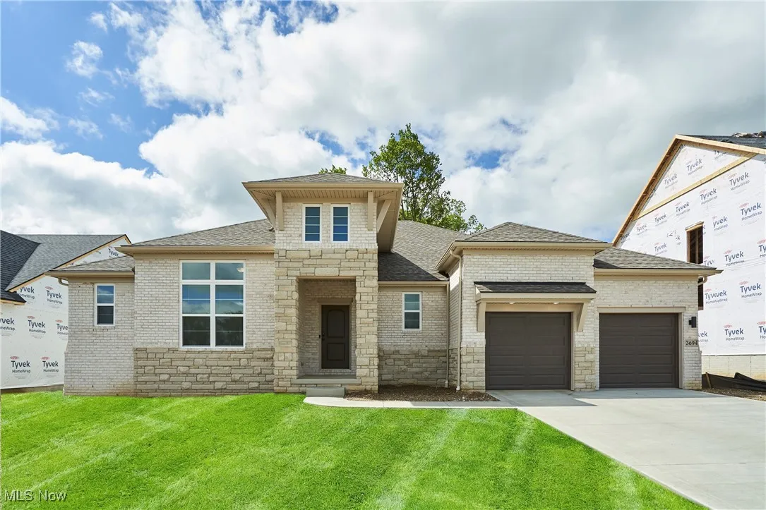 View of front of house featuring an attached garage, roof with shingles, driveway, a front lawn, and stone siding