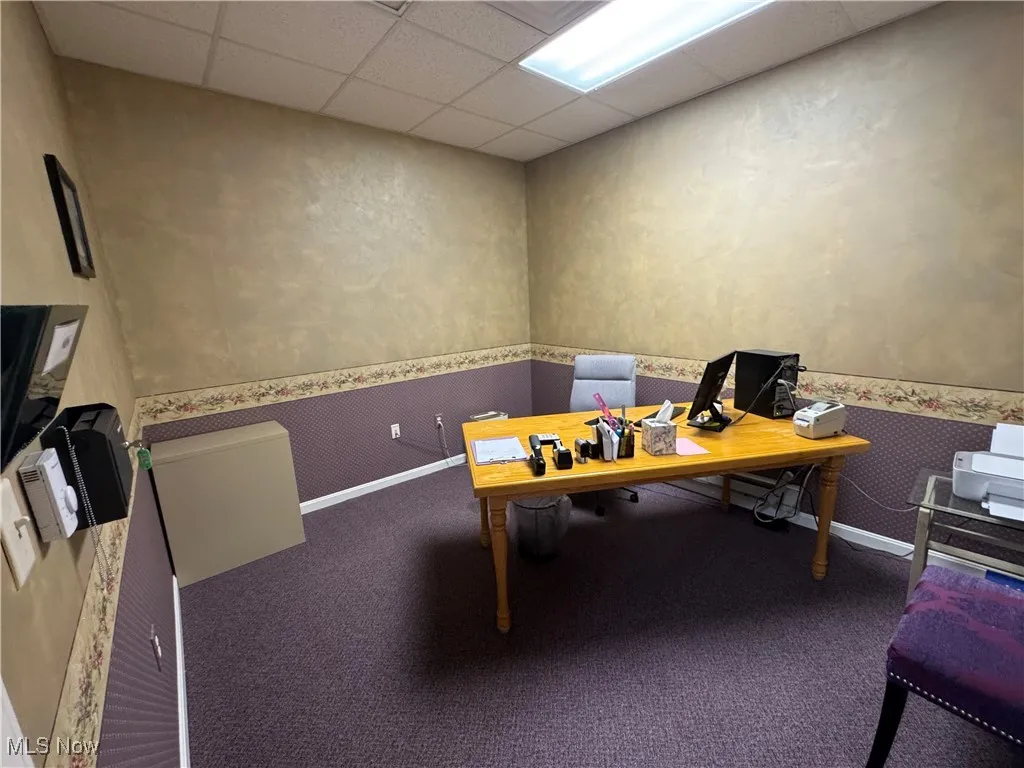 Carpeted office featuring a paneled ceiling, wallpapered walls, and baseboards