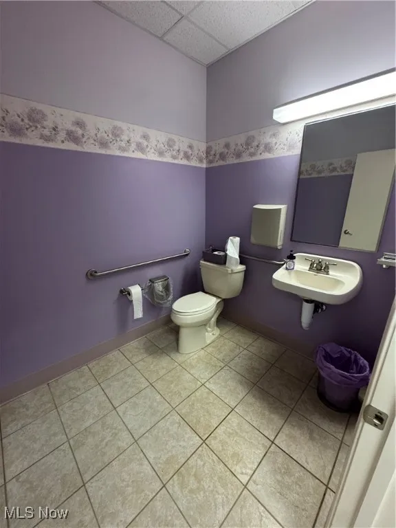 Bathroom with a paneled ceiling, toilet, a sink, and tile patterned flooring