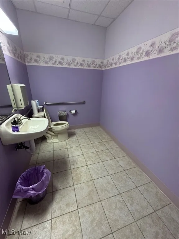 Bathroom with toilet, a sink, tile patterned floors, a drop ceiling, and baseboards
