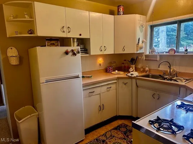 Kitchen featuring freestanding refrigerator, a sink, backsplash, and open shelves