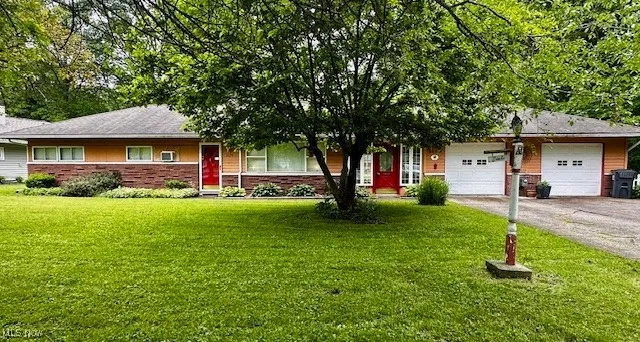 Ranch-style home featuring driveway, an attached garage, a front lawn, and brick siding