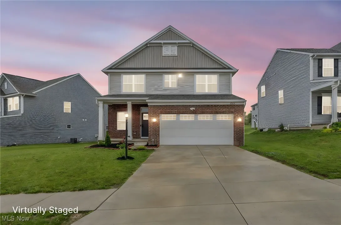View of front of property with brick siding, a garage, a front lawn, driveway, and board and batten siding