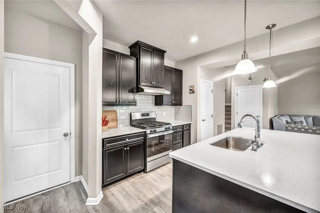 Kitchen featuring gas range, a sink, light wood-style floors, backsplash, and hanging light fixtures
