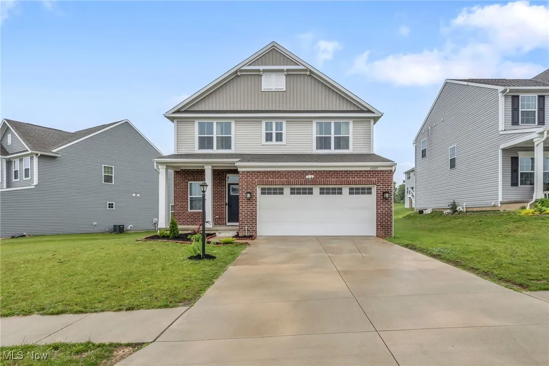 View of front of property with brick siding, board and batten siding, an attached garage, and a front yard