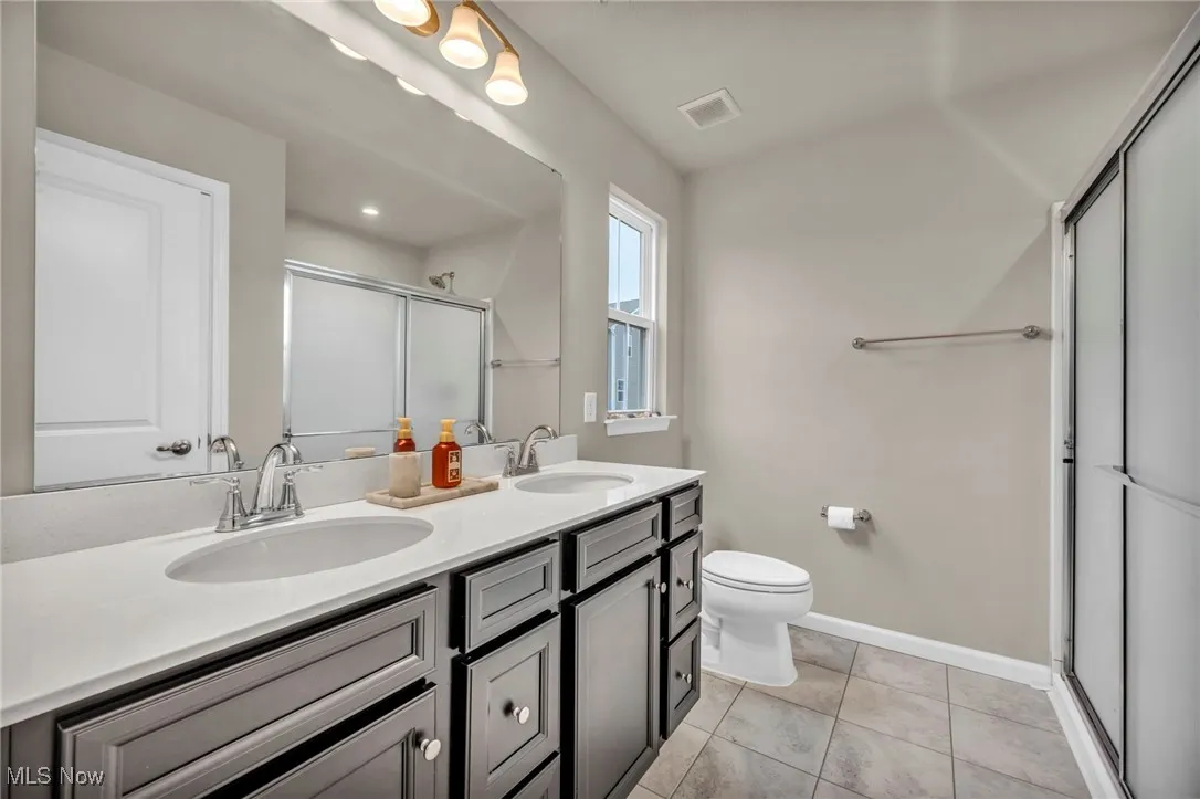 Full bath featuring a shower stall, double vanity, toilet, baseboards, and tile patterned floors