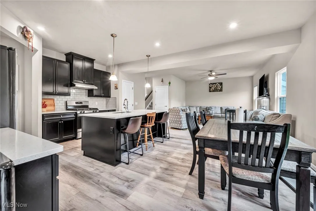 Kitchen featuring gas stove, dark cabinets, ceiling fan, a kitchen bar, and recessed lighting