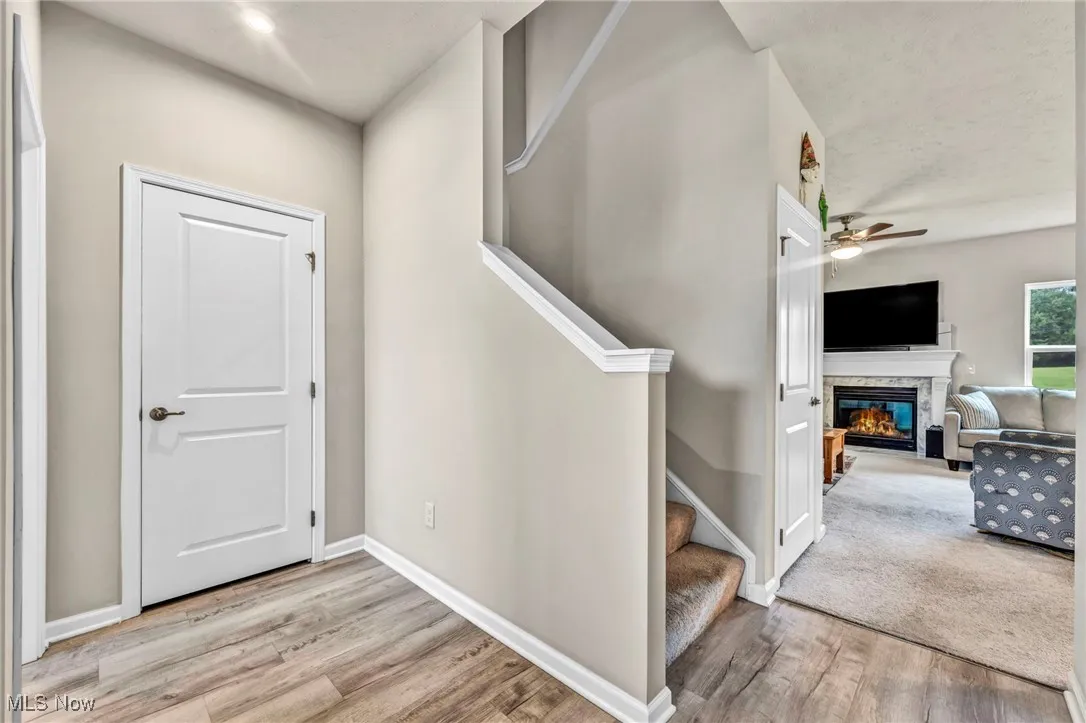 Stairs with wood finished floors, a glass covered fireplace, a ceiling fan, and baseboards