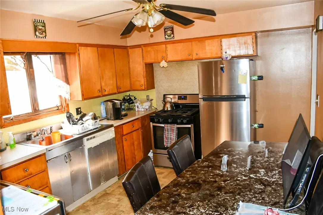 Kitchen with stainless steel appliances, a ceiling fan, backsplash, and brown cabinets