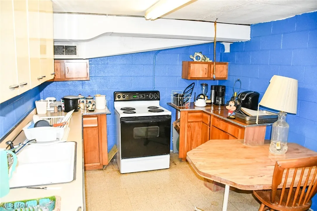 Kitchen featuring white electric stove, a sink, light flooring, brown cabinetry, and concrete block wall