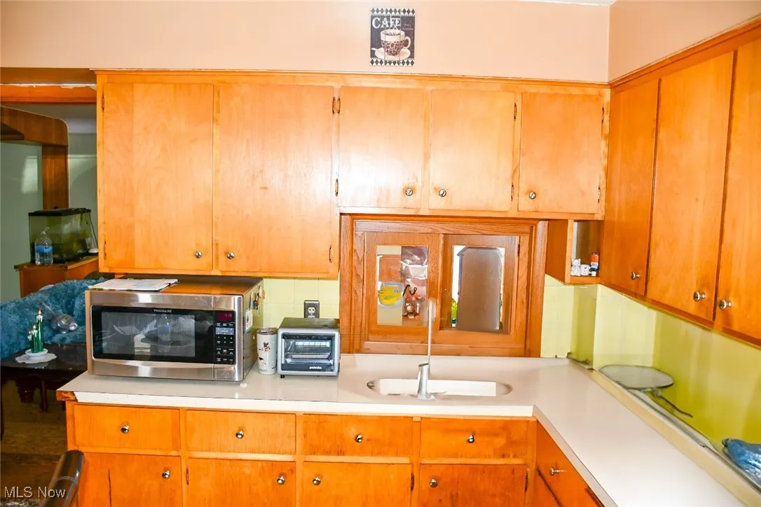 Kitchen with stainless steel microwave, light countertops, a sink, and brown cabinets