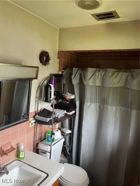 Full bath featuring toilet, vanity, curtained shower, and tile walls