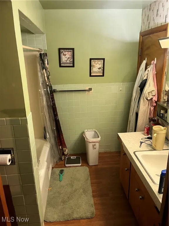 Bathroom with tile walls, wood finished floors, vanity, wainscoting, and shower / bath combination with curtain
