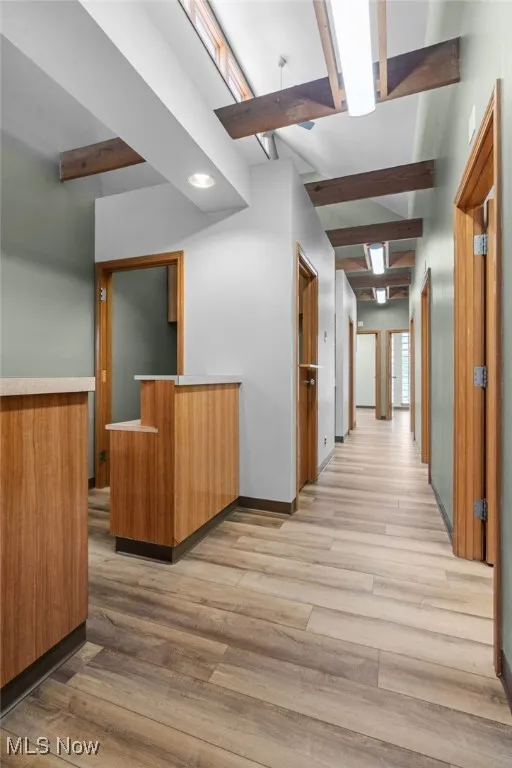 Hall featuring light wood-style flooring, baseboards, and beam ceiling