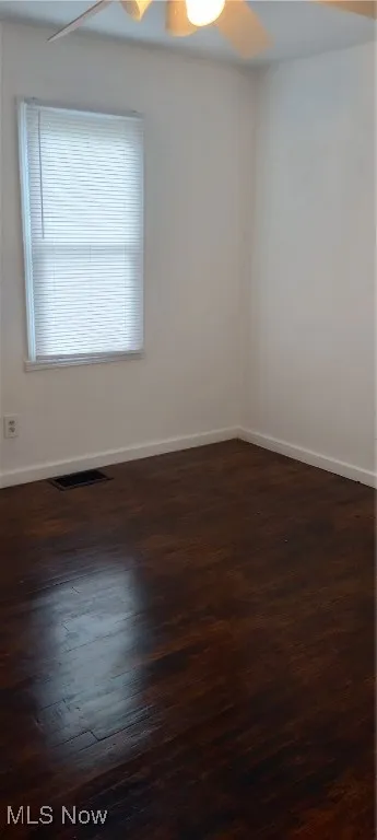 Spare room with dark wood-style floors, a ceiling fan, and baseboards