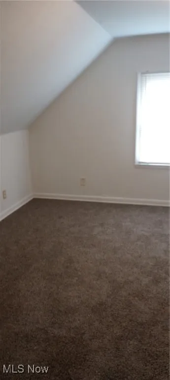 Additional living space featuring vaulted ceiling, dark colored carpet, and baseboards