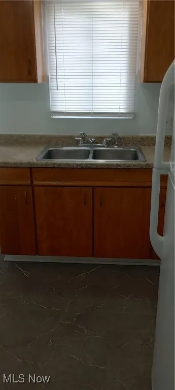 Kitchen with refrigerator, a sink, brown cabinetry, light countertops, and dark marble finish floors