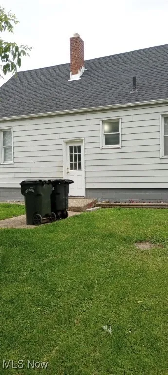 Back of property with a yard, a shingled roof, and a chimney