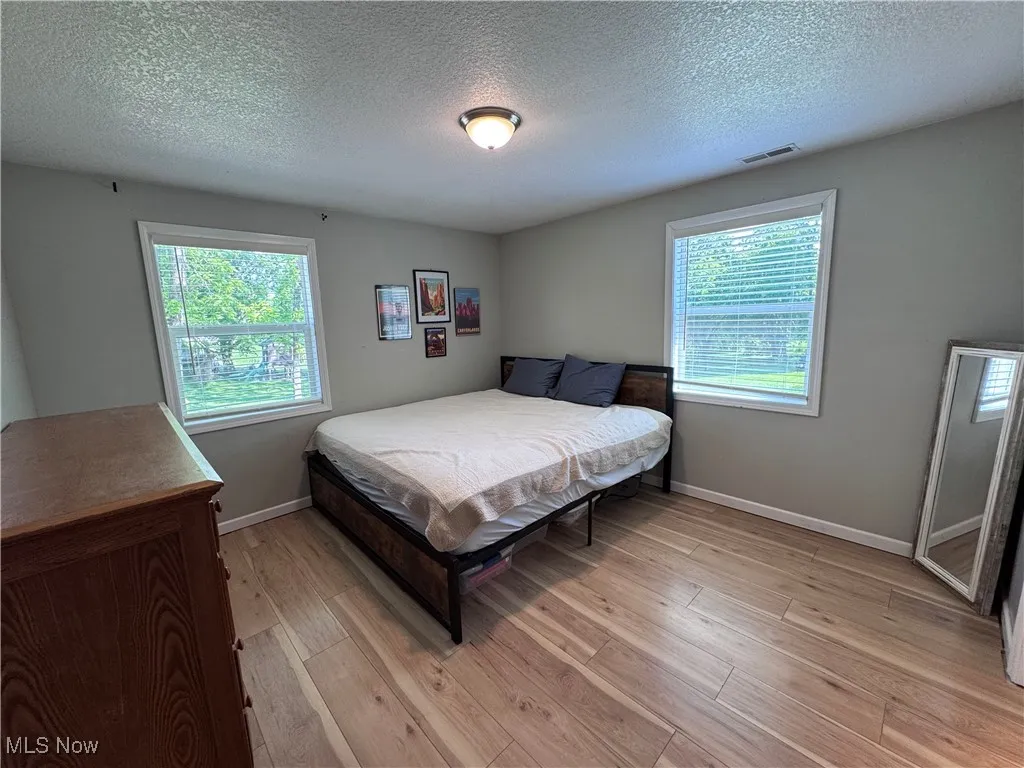 Bedroom with light wood-style floors, a textured ceiling, and baseboards