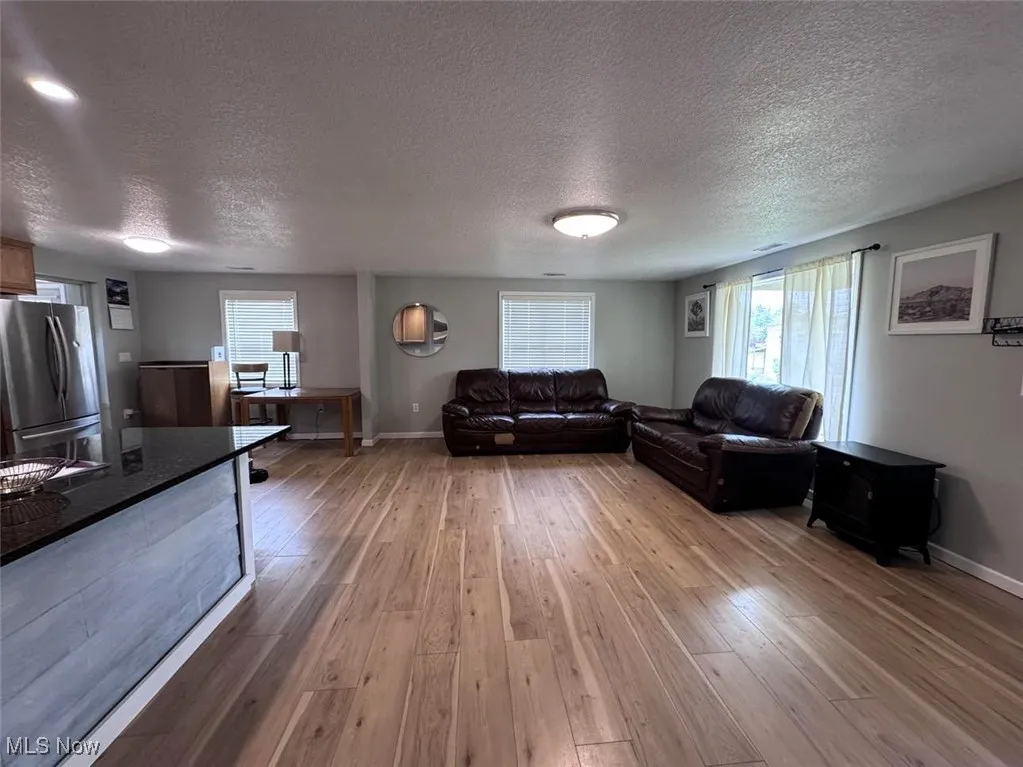Living room with light wood-style floors, a textured ceiling, and baseboards