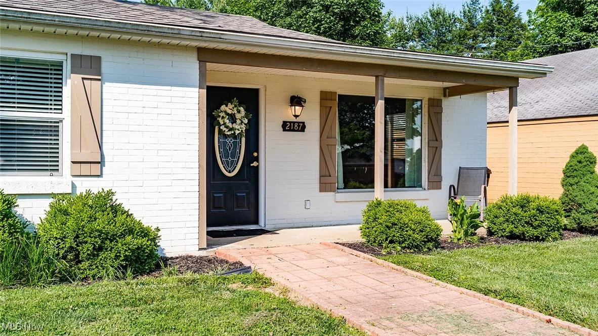 Doorway to property featuring brick siding, a shingled roof, covered porch, and a yard