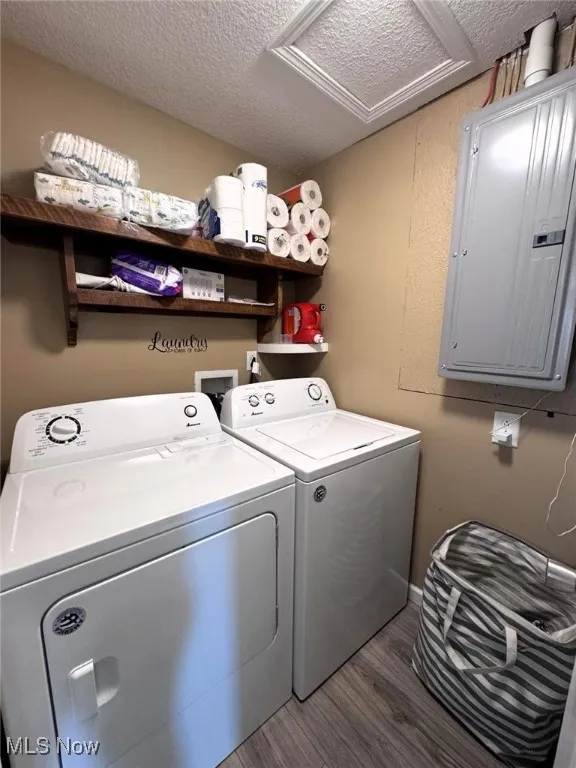 Washroom featuring electric panel, washing machine and dryer, attic access, wood finished floors, and a textured ceiling