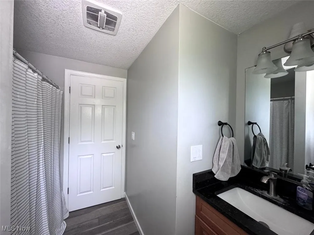 Bathroom with a textured ceiling, wood finished floors, vanity, and baseboards