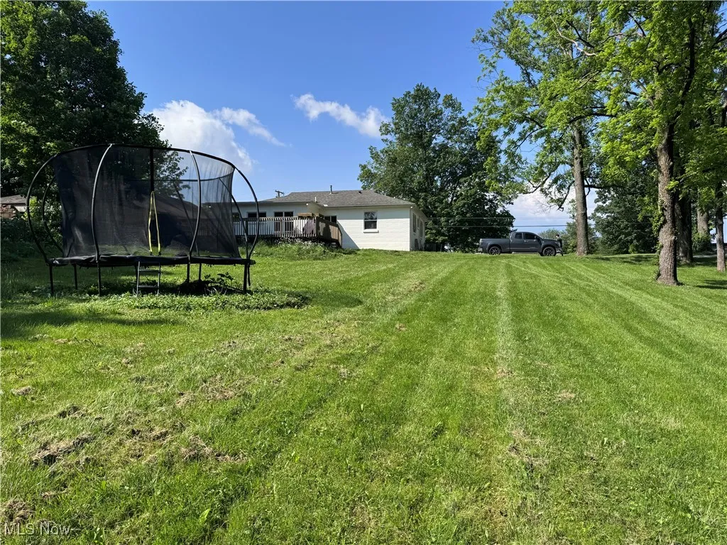 View of green lawn featuring a trampoline and a wooden deck