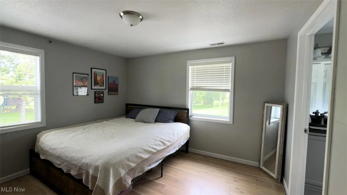 Bedroom with multiple windows, baseboards, light wood-style floors, and a textured ceiling