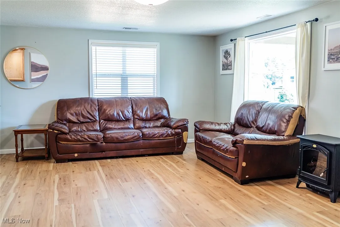 Living area featuring light wood-type flooring, a wood stove, healthy amount of natural light, and a textured ceiling