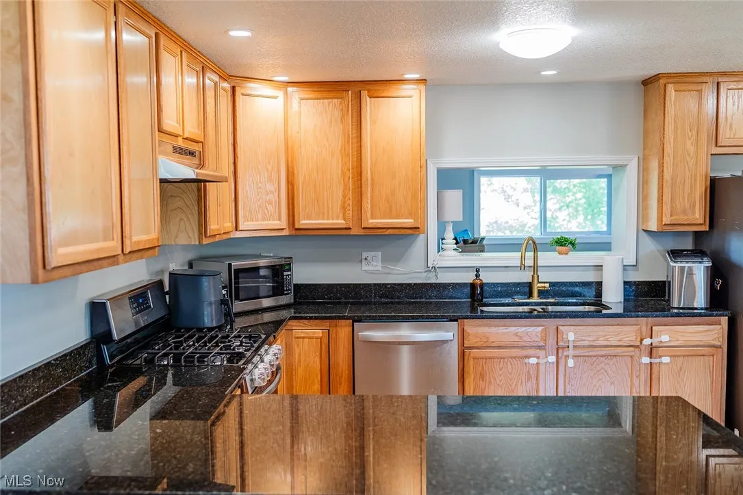 Kitchen with stainless steel appliances, under cabinet range hood, dark stone countertops, and recessed lighting
