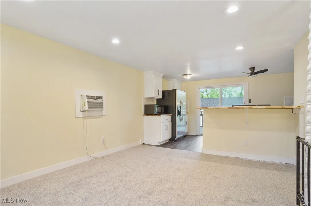 Unfurnished living room with dark colored carpet, an AC wall unit, baseboards, recessed lighting, and a ceiling fan
