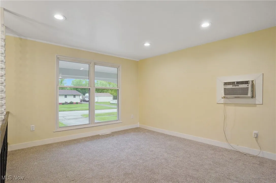 Unfurnished room featuring an AC wall unit, recessed lighting, light colored carpet, baseboards, and crown molding