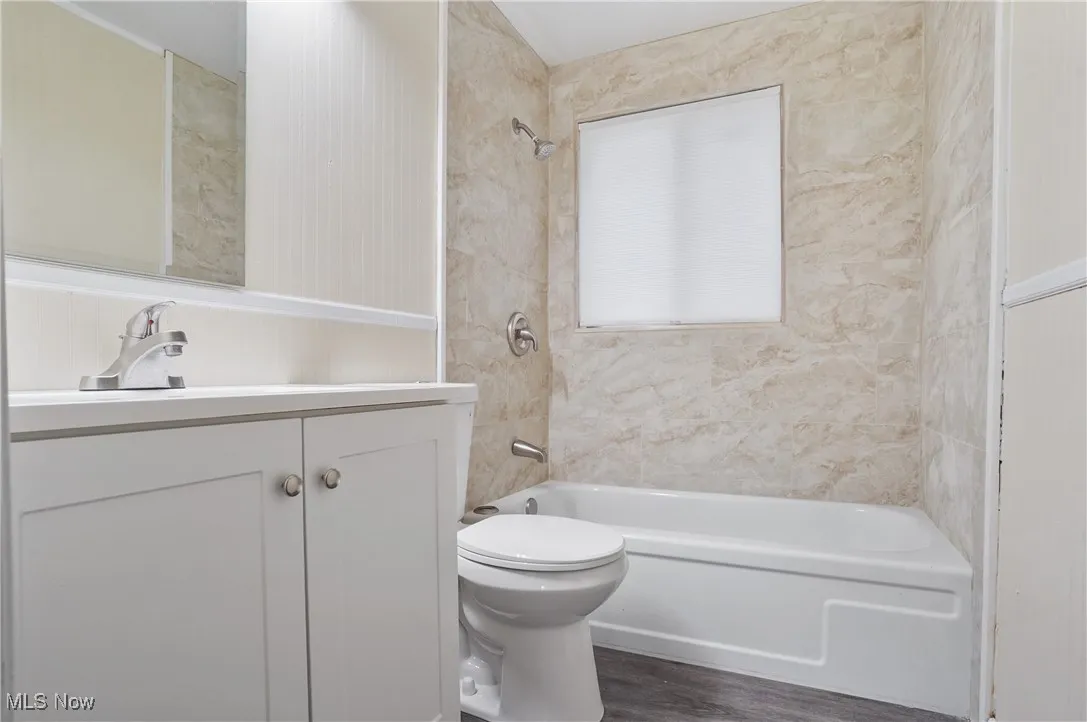 Bathroom with vanity, shower / bath combination, toilet, and wood finished floors