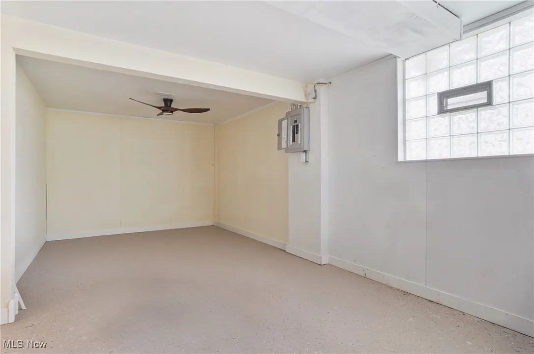 Empty room featuring ceiling fan, baseboards, speckled floor, and electric panel