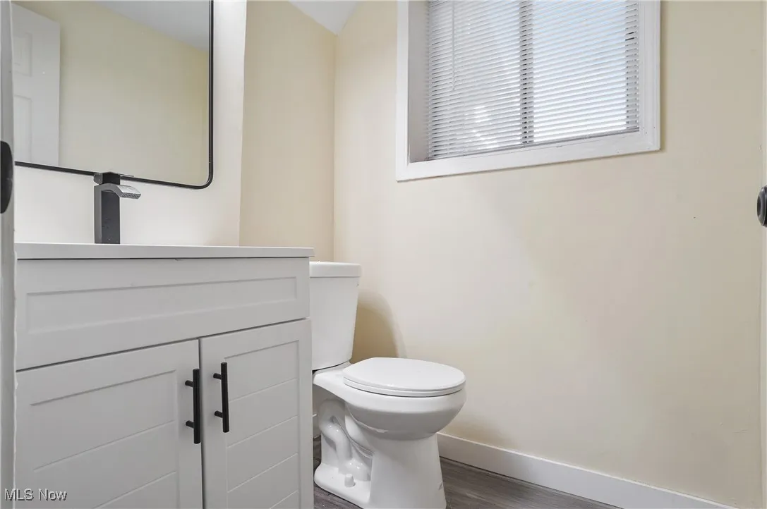 Half bath with wood finished floors, baseboards, toilet, and vanity