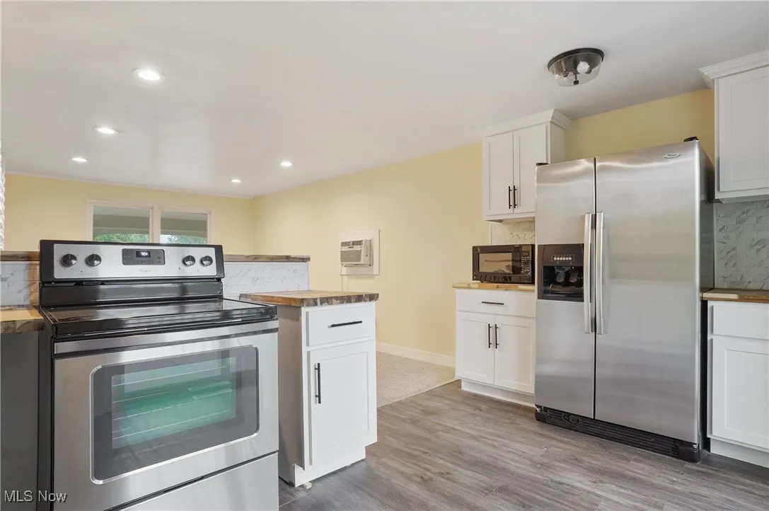 Kitchen with stainless steel appliances, decorative backsplash, light wood-style flooring, white cabinets, and wood counters