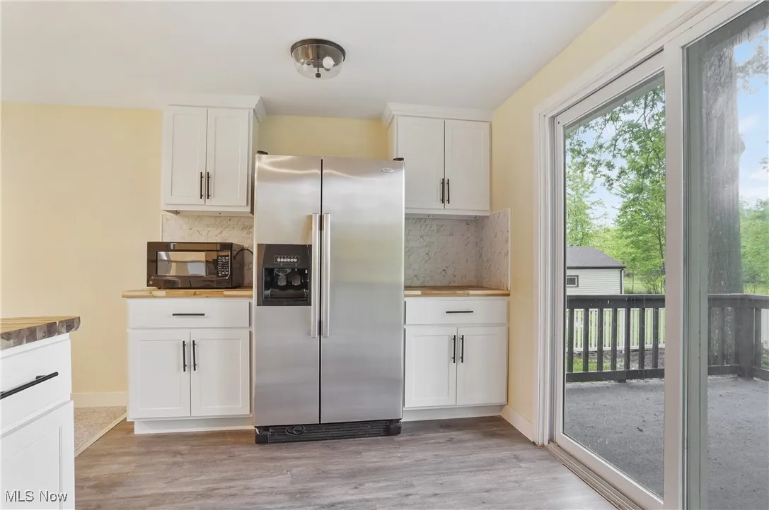 Kitchen with stainless steel refrigerator with ice dispenser, black microwave, backsplash, and white cabinetry