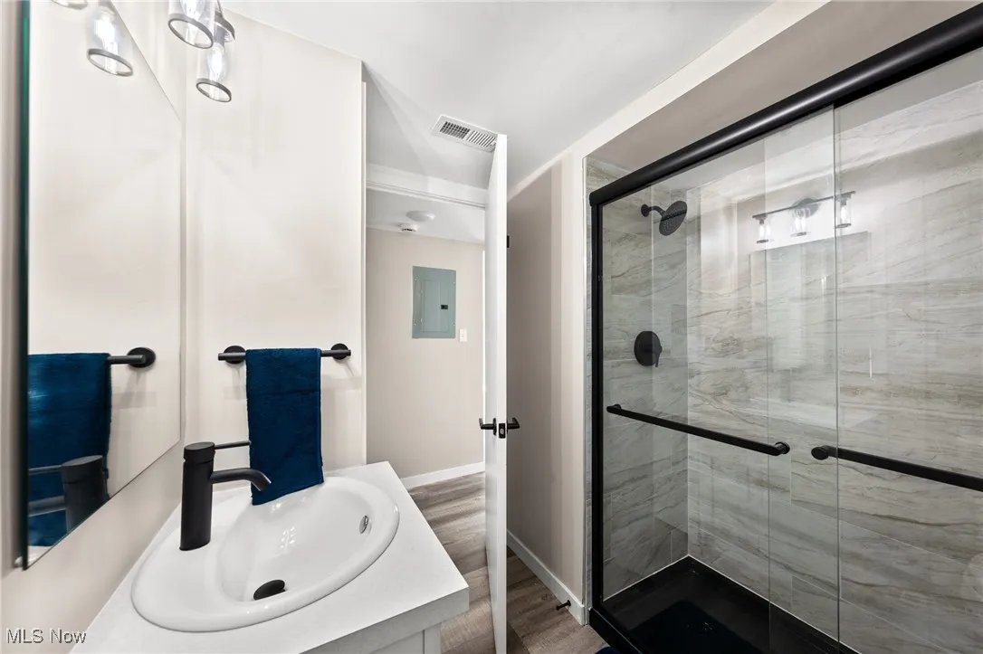 Bathroom with electric panel, a stall shower, vanity, baseboards, and wood finished floors