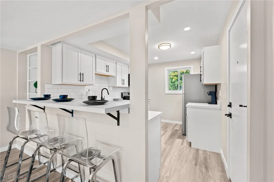 Kitchen with a kitchen bar, a peninsula, light wood finished floors, white cabinets, and light countertops