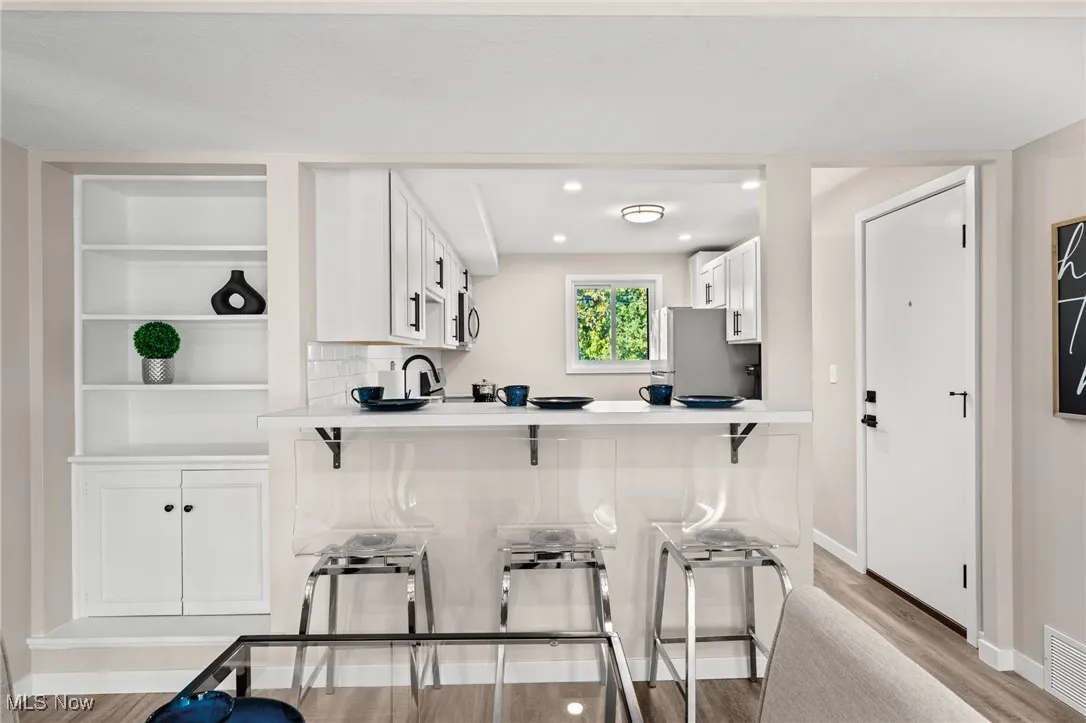 Kitchen featuring stainless steel appliances, light wood finished floors, a breakfast bar, white cabinets, and a peninsula