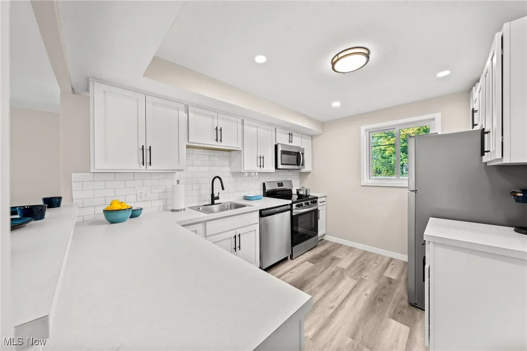 Kitchen featuring appliances with stainless steel finishes, a sink, white cabinets, backsplash, and light countertops
