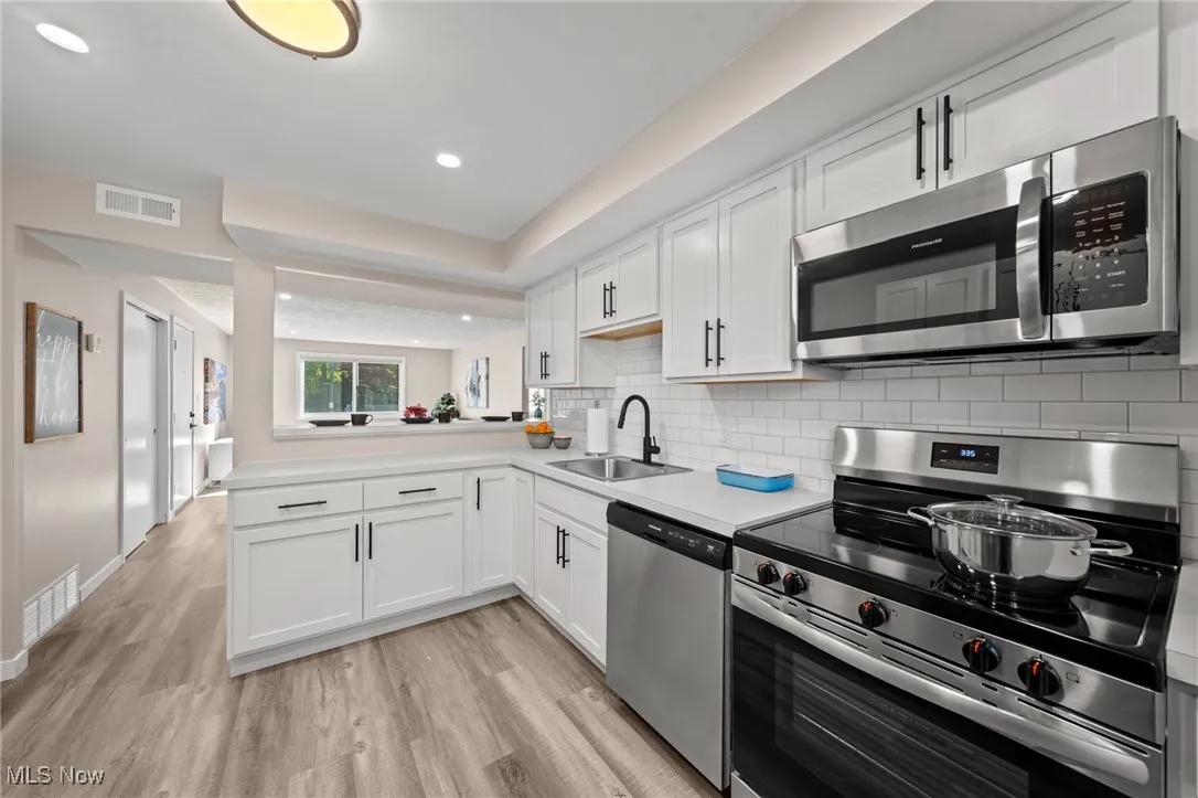 Kitchen with stainless steel appliances, a sink, light wood finished floors, white cabinets, and recessed lighting