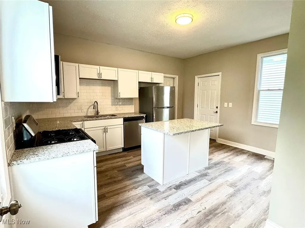 Kitchen featuring stainless steel appliances, a sink, backsplash, wood finished floors, and a textured ceiling