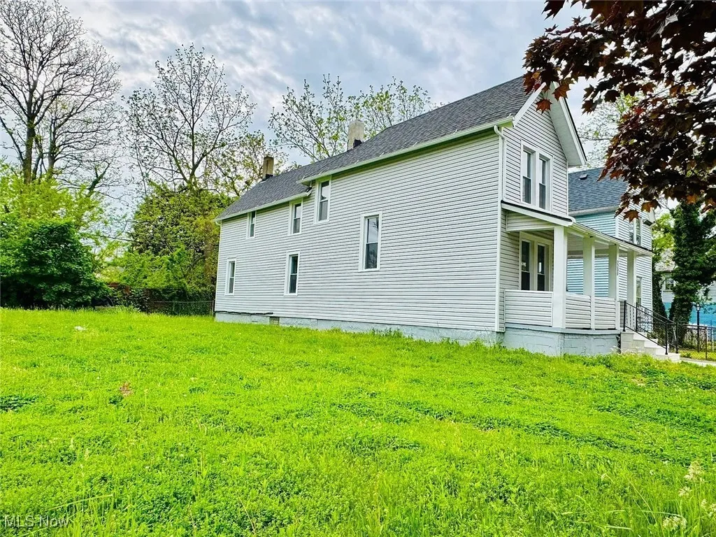 View of side of property with a chimney, covered porch, a shingled roof, and a yard
