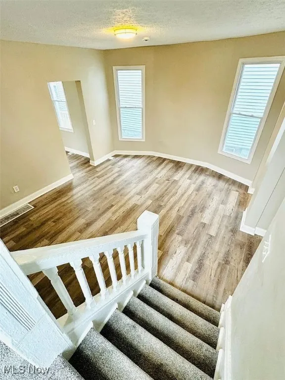 Stairs with baseboards, wood finished floors, and a textured ceiling