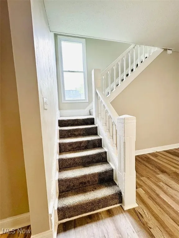 Staircase with wood finished floors, baseboards, and a textured ceiling